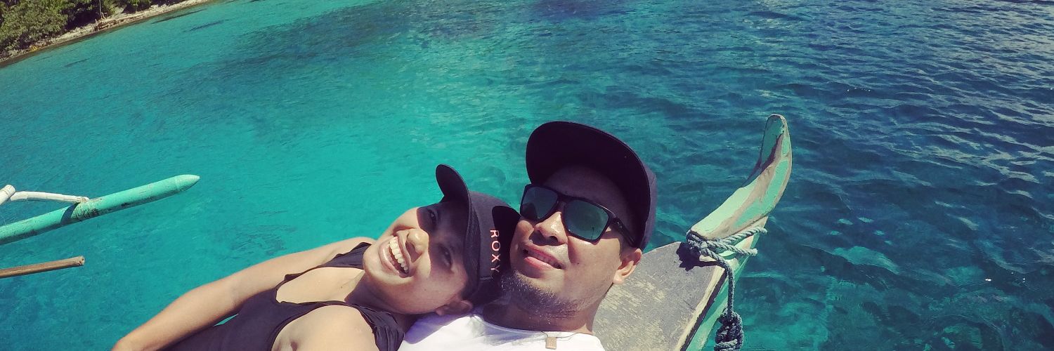 Batang Dagat — the couple resting on the bow of an outrigger banca over turquoise reef water